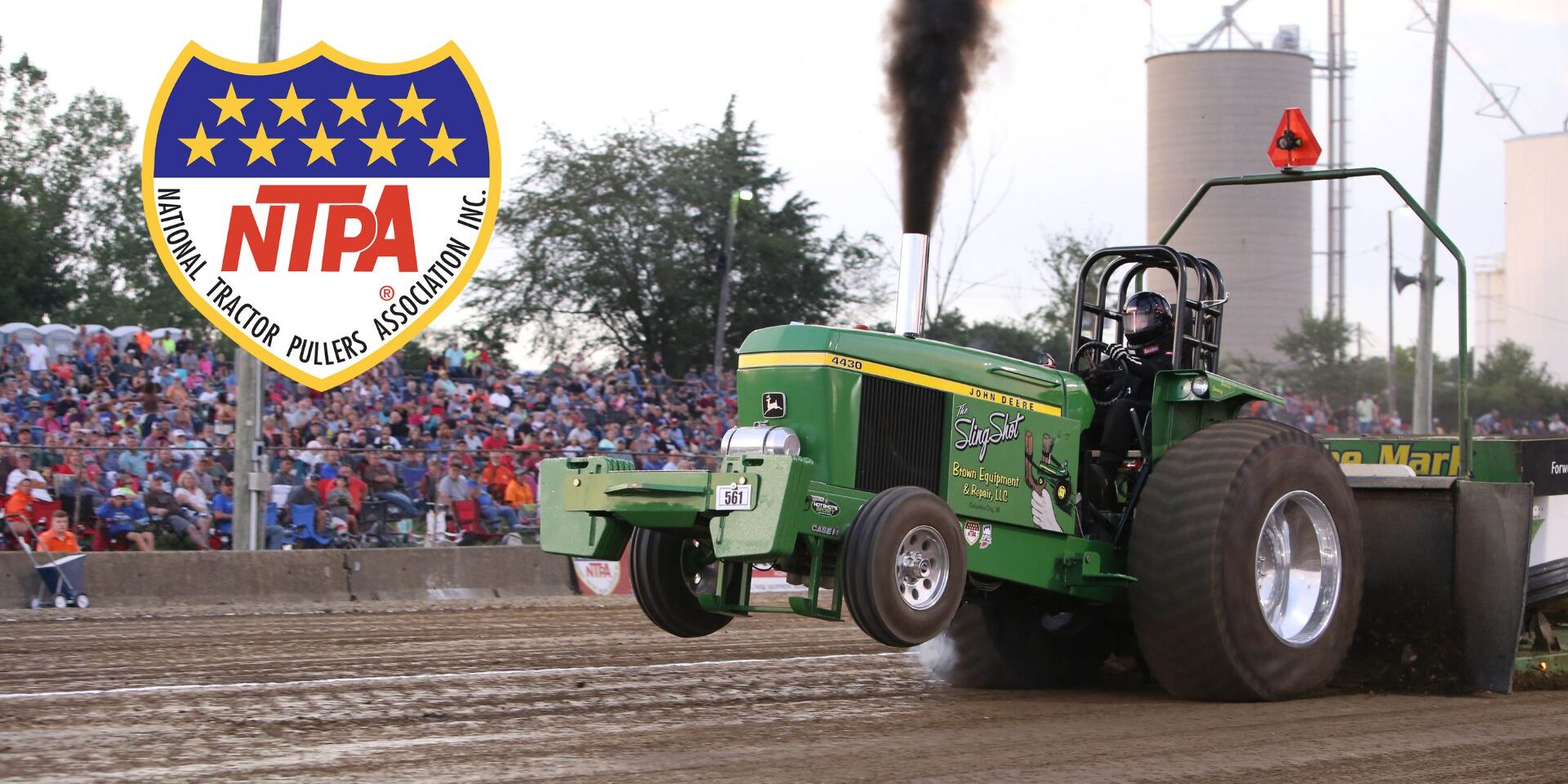 Photograph of John Deere tractor pulling down a dirt track with NTPA logo.