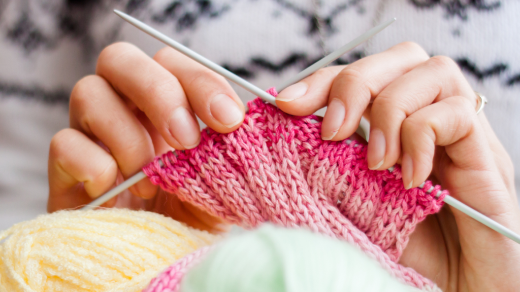 Hands knitting pink fabric.