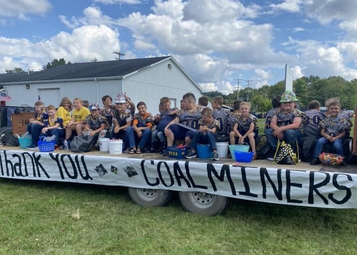 Photograph of youth football players on a trailer bed with a sign that says Thank You Coal Miners.
