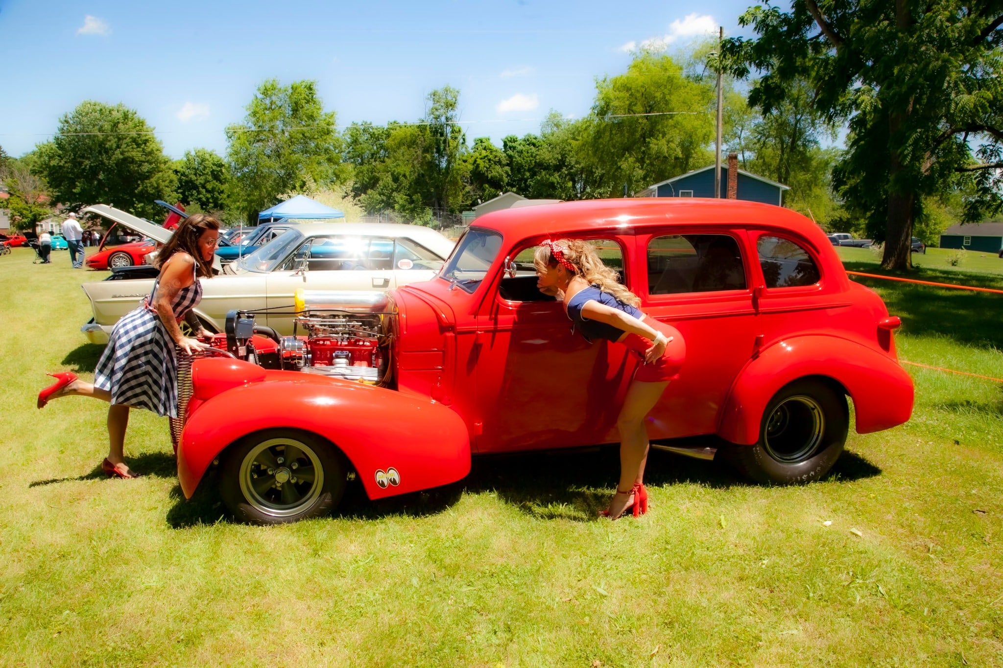 Photograph of 3 pin-up girls in front of a red car at the American Legion Cruise-In for Veterans.