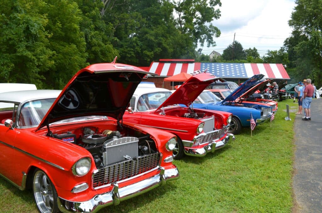 Photograph of the VFW's Freedom Car Show with two red and one blue cars in front of an American Flag roof.