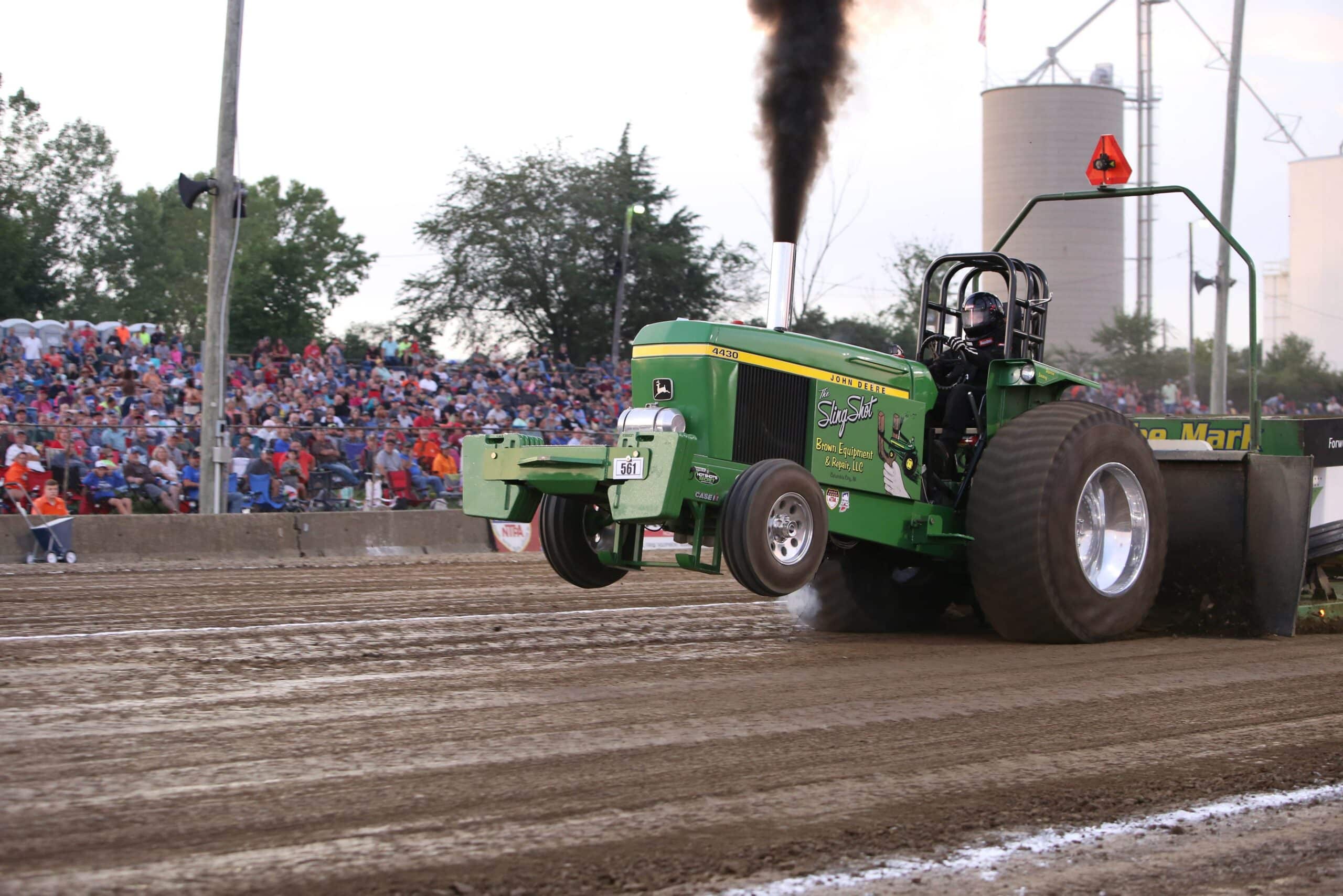 Photograph by NTPA of a John Deere tractor pulling down a dirt track in front of a grandstand audience.