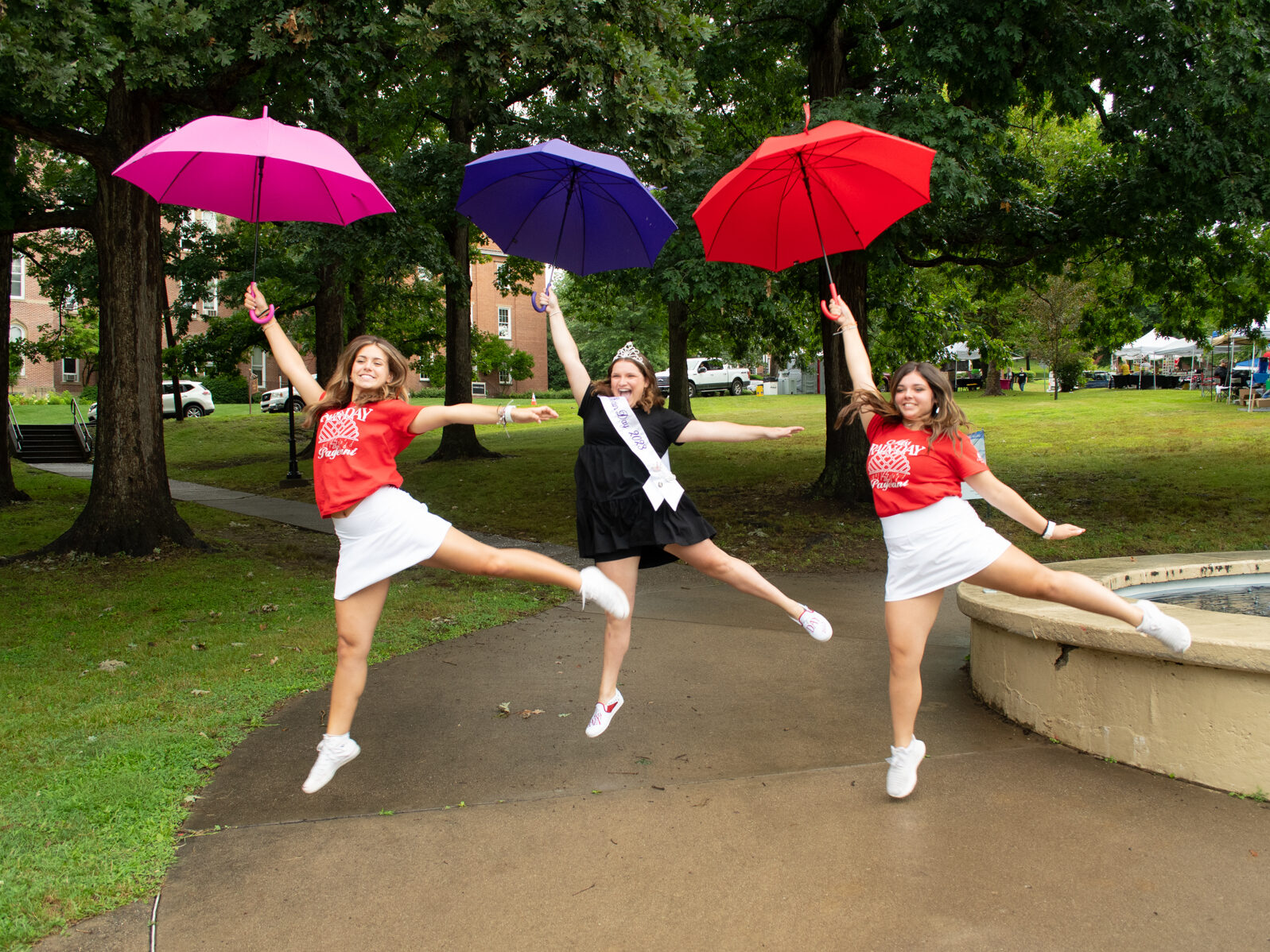 Photograph of three female teenagers jumping while holding an umbrella.