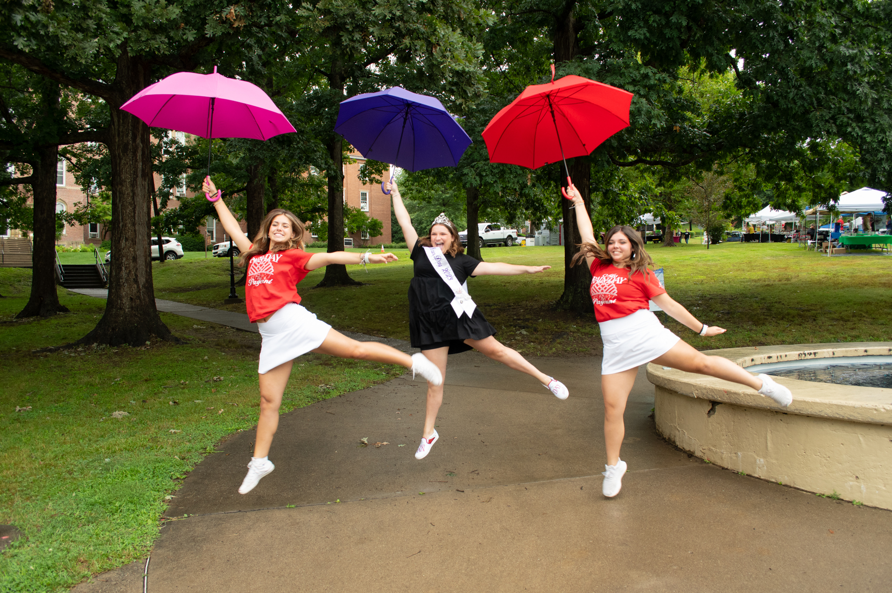 Photograph of three female teenagers jumping while holding an umbrella.