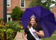 Photograph of Miss Rain Day 2023, Abby Ray, with a purple umbrellas beside a basket of marigolds and ferns.