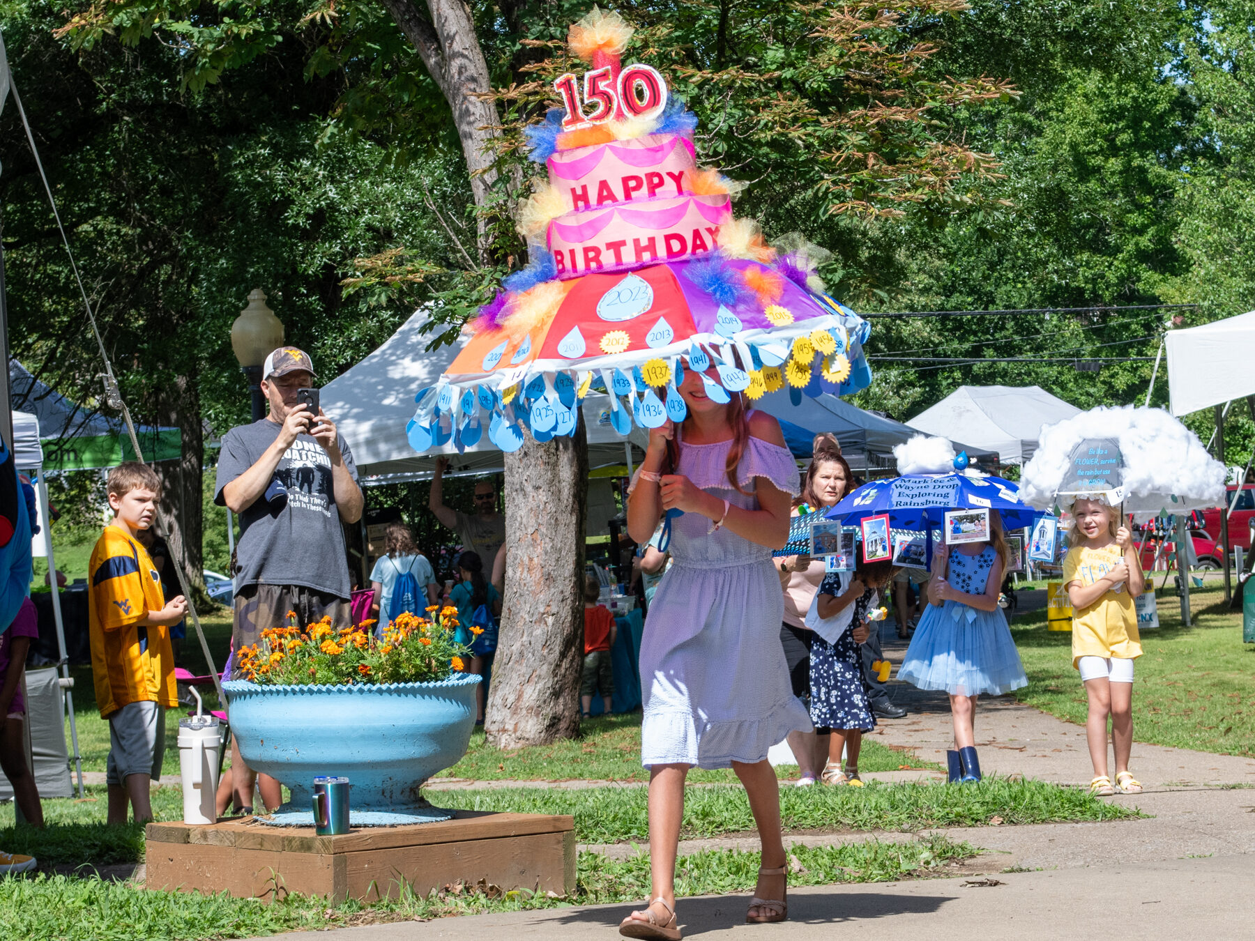 Photograph of a female child carrying a decorated umbrella to look like a cake celebrating the 150th birthday of Rain Day in Waynesburg, Pennsylvania.