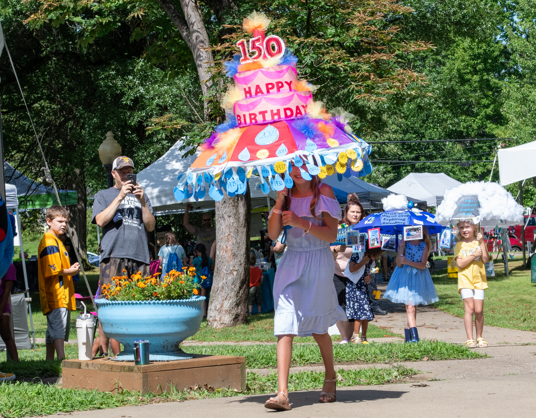 Photograph of a female child carrying a decorated umbrella to look like a cake celebrating the 150th birthday of Rain Day in Waynesburg, Pennsylvania.