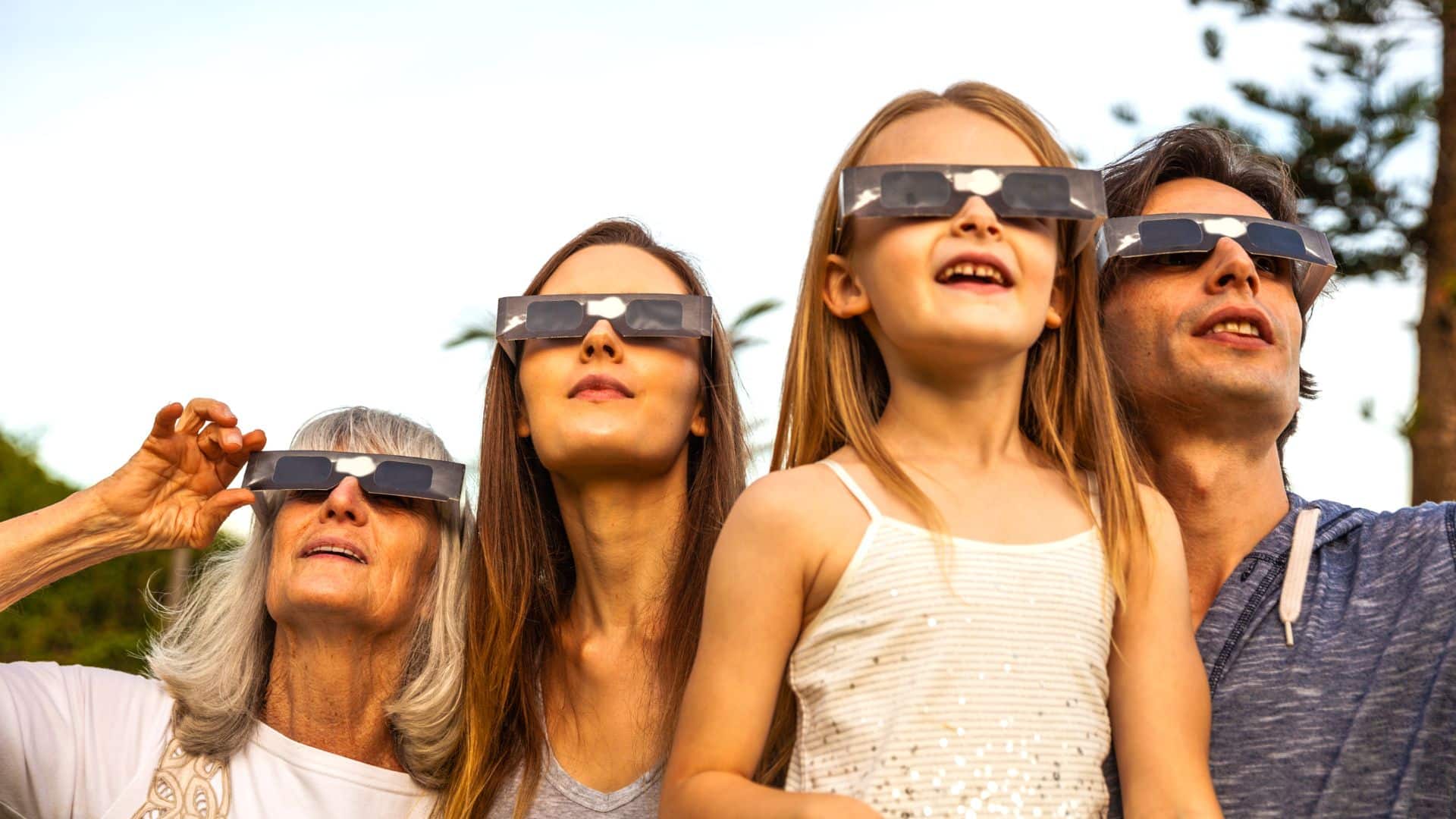 Photograph of a family looking up at the sky wearing solar eclipse glasses.