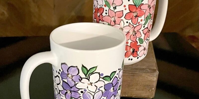 Photograph of two white mugs painted with purple and red flowers.