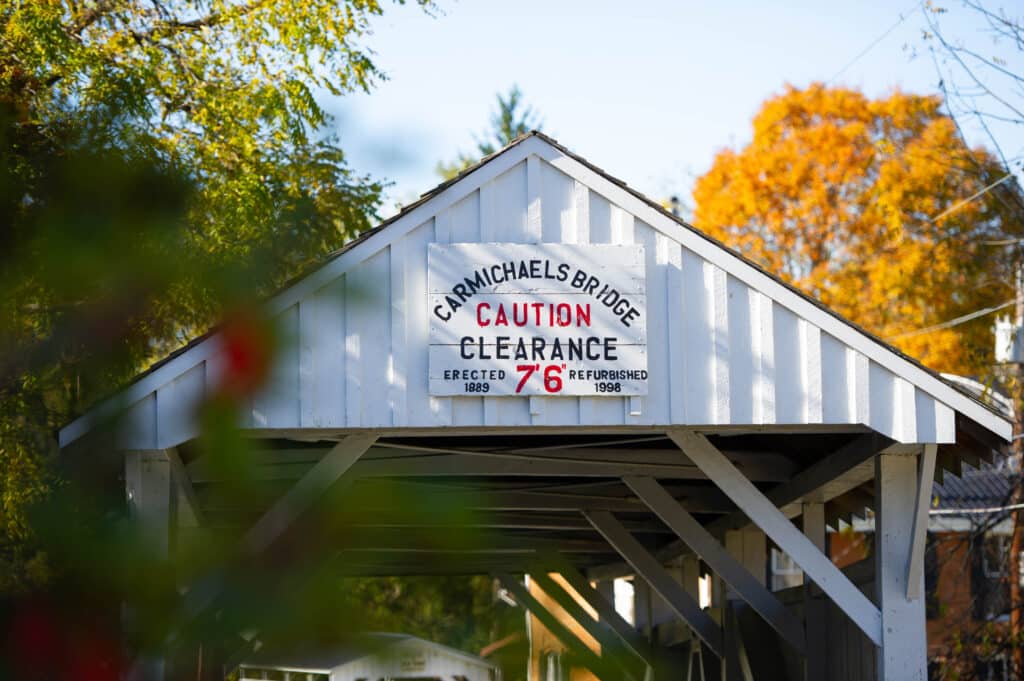 Carmichaels Bridge covered bridge with caution clearance sign surrounded by colorful fall foliage.