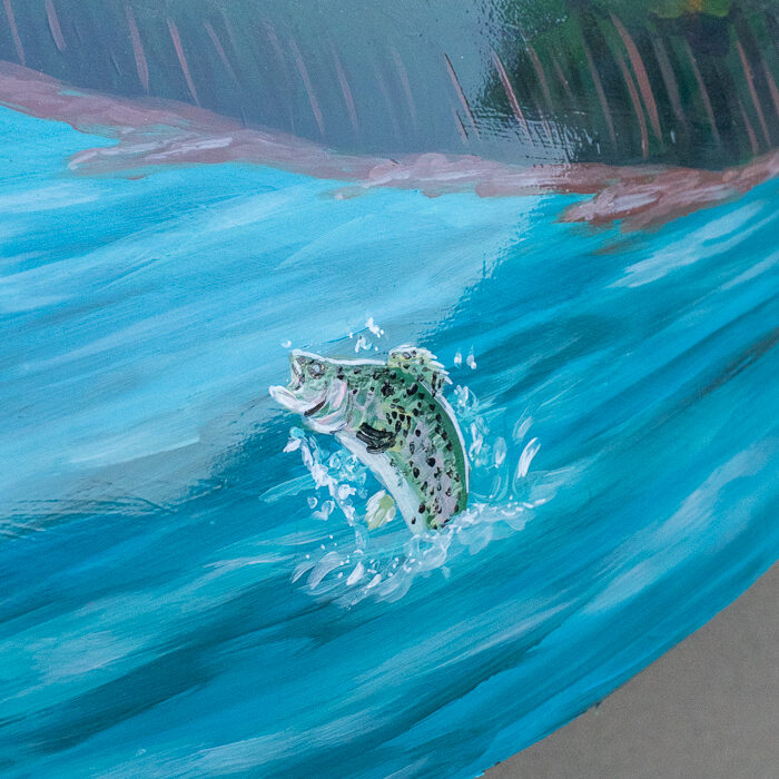 Close-up of a painted trout leaping from a bright blue river with a forested shoreline in the background.
